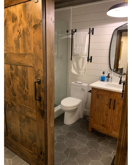 Rustic bathroom featuring reclaimed wood vanity, hexagonal tile flooring, glass shower, white shiplap walls, and barn door...