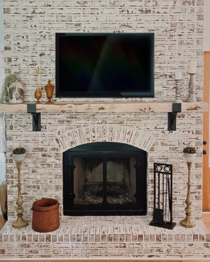 Black metal mantel bracket with square support bar mounted on whitewashed brick fireplace supporting wooden mantel shelf -...