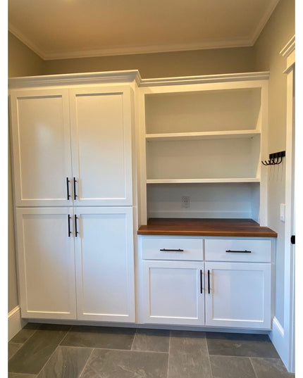 White shaker-style built-in cabinets with wood countertop, open shelving, and black hardware in mudroom with gray tile flo...