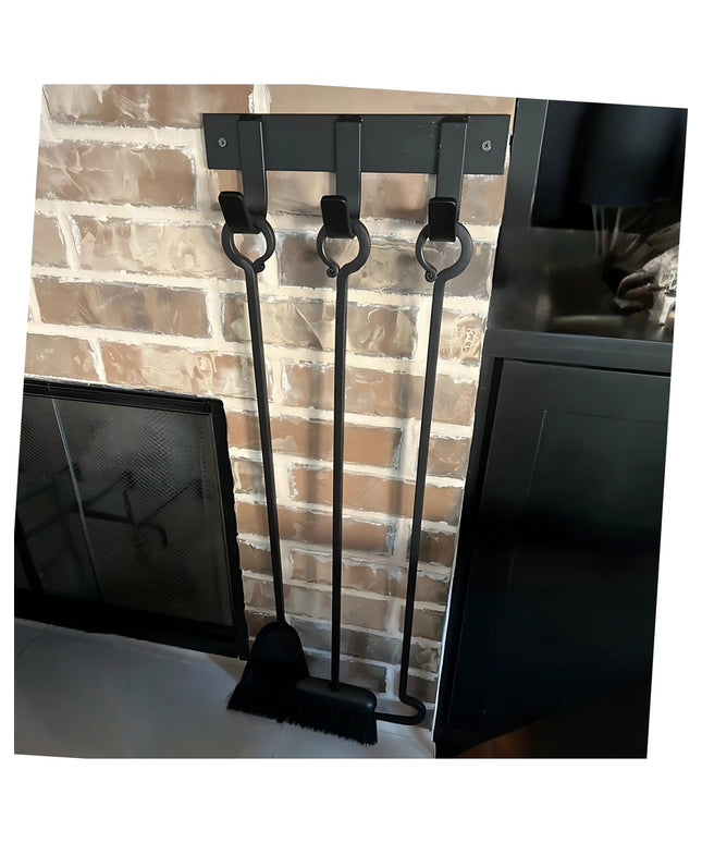Black metal Mary Style Handmade Coat Rack by Industrial Farm Co with three wall-mounted hooks holding fireplace tools agai...