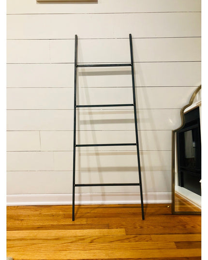 Black metal Tapered Michael Farmhouse Ladder by Industrial Farm Co leaning against white shiplap wall on hardwood floors