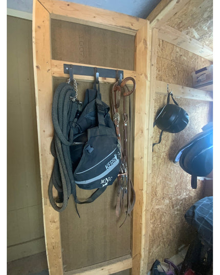 Industrial Farm Co Camillus Style black metal coat rack mounted in wooden frame holding horse tack, ropes, and riding equi...
