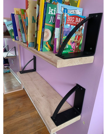 Black triangular Brie Bookshelf Brackets by Industrial Farm Co supporting wooden shelves with children's books on purple wall