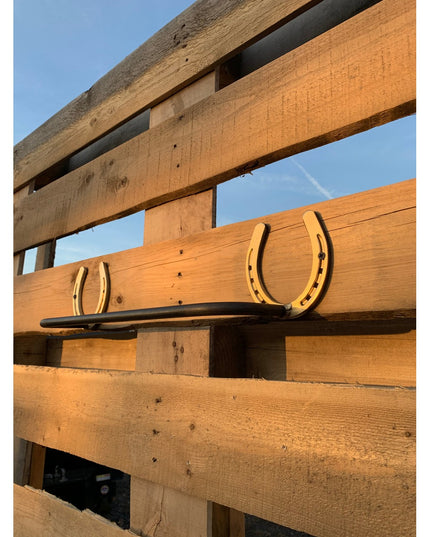 Rustic golden horseshoe towel bar mounted on weathered wood fence, The Donahue Horseshoe Blanket & Towel Bar by Industrial...