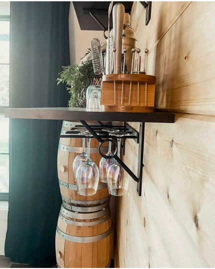 The White Plains Wine Glass Rack by Industrial Farm Co mounted under wooden shelf holding wine glasses above wooden barrel...