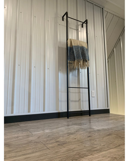 Black metal Hal Standing Mounted Blanket Ladder by Industrial Farm Co displaying cream and blue fringed throw blanket agai...
