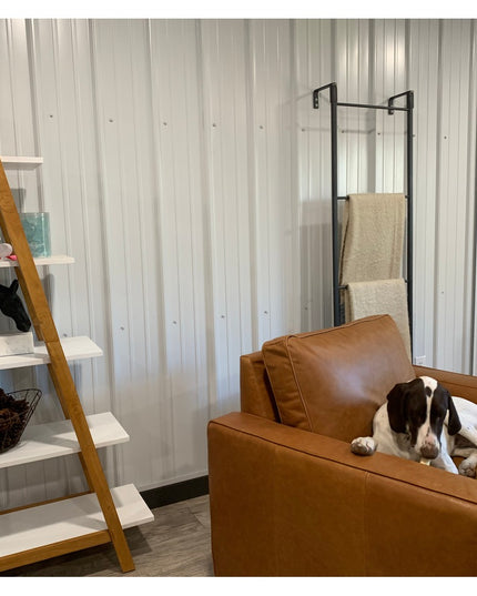 Black metal standing blanket ladder with beige towels displayed in modern living room next to brown leather chair and wood...