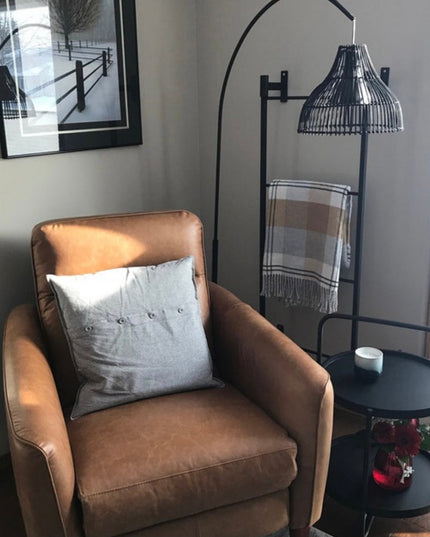 Black metal wall-mounted Ossit ladder by Industrial Farm Co displayed next to tan leather armchair with gray pillow and ar...