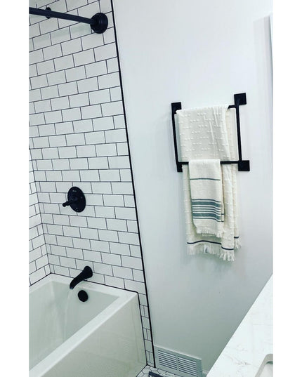 Black metal Parker Hand Towel Holder ladder mounted on white bathroom wall with cream towels, next to white subway tile sh...