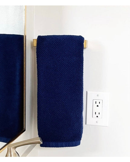 Navy blue towel hanging on brass gold Emma Towel Holder door pull mounted on white bathroom wall next to electrical outlet