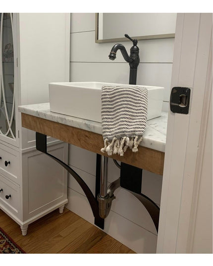Black metal Rochester countertop support brackets holding wooden floating vanity with white vessel sink in modern farmhous...