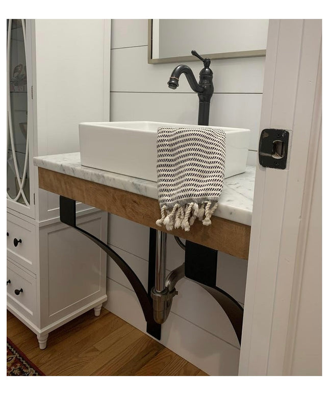 Black metal Rochester countertop support brackets holding wooden floating vanity with white vessel sink in modern farmhous...
