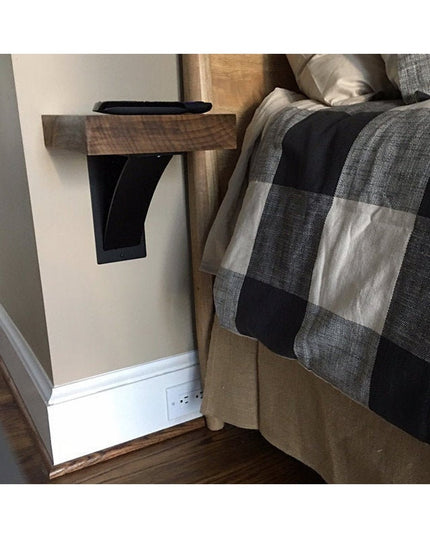 Black steel Ninemile 5-inch industrial shelf bracket with curved support bar mounted under wooden bedside table next to bed