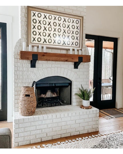 Black metal Kudlick Farmhouse Mantel Brackets supporting rustic wood beam on white brick fireplace by Industrial Farm Co