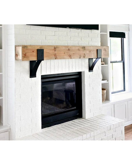 Black metal Kudlick Farmhouse Mantel Brackets supporting reclaimed wood beam above white brick fireplace with built-in she...