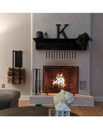 Black metal Toby Firewood Holder by Industrial Farm Co mounted on wall next to white brick fireplace holding stacked logs