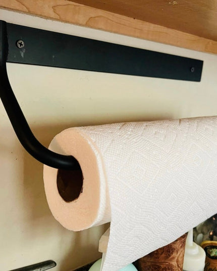 Black metal Hyde Hall Paper Towel Holder by Industrial Farm Co mounted under cabinet with white paper towel roll in modern...