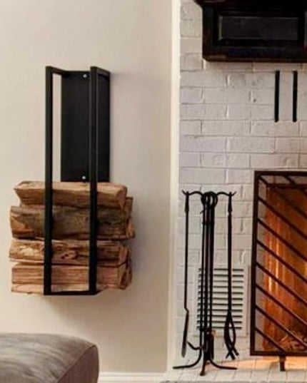 Black metal Toby Firewood Holder by Industrial Farm Co mounted on white wall holding stacked firewood logs next to brick f...