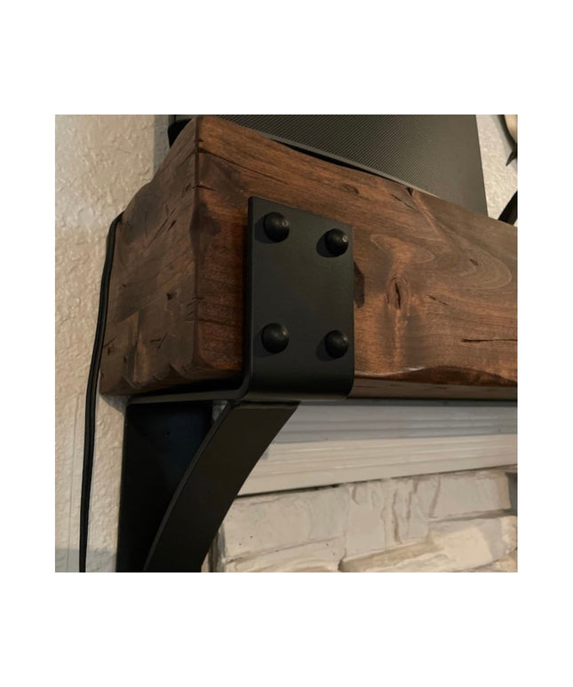 Heavy duty black steel Spafford mantel bracket with decorative rivets supporting reclaimed wood beam above white brick fir...