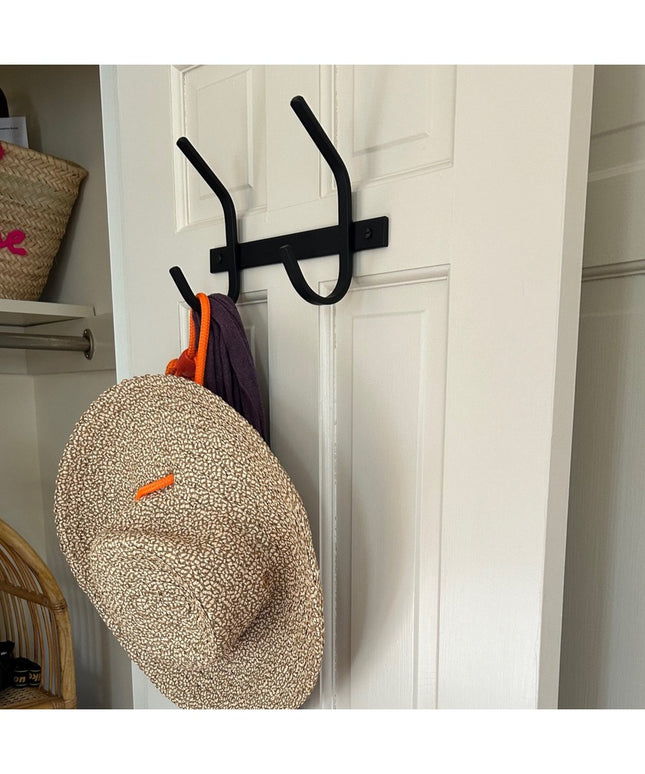 Black metal Meredith Petite Double J Coat Rack by Industrial Farm Co mounted on white door with woven hat and clothing