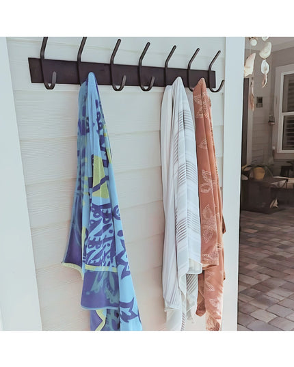 Cooperstown Double Hook Coat Rack by Industrial Farm Co mounted on white shiplap wall with colorful towels and clothing ha...