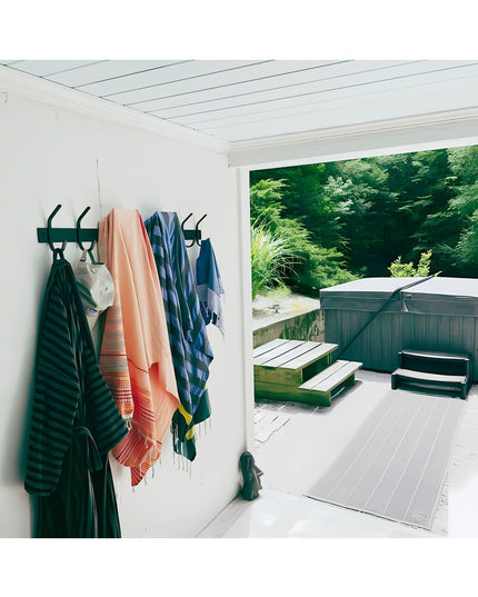 The Cooperstown Double Hook black metal coat rack mounted on white wall with colorful towels hanging, outdoor pool area vi...