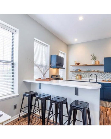 Modern kitchen with white countertop supported by heavy duty steel shelf brackets, featuring black metal bar stools and bl...