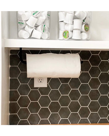 Black metal Hyde Hall Paper Towel Holder mounted under white kitchen cabinet above hexagon tile backsplash with coffee pod...