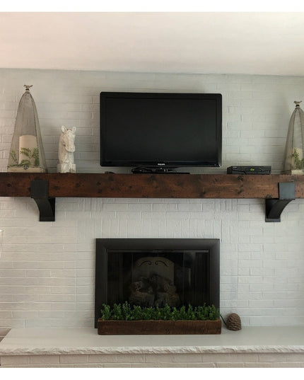 Rustic wooden mantel shelf with black Norfolk Farmhouse Brackets by Industrial Farm Co mounted above white brick fireplace...