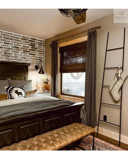 Black metal tapered farmhouse ladder by Industrial Farm Co displayed in rustic bedroom with brick wall and wooden bed frame