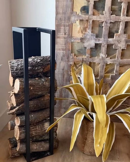 Black metal Toby Firewood Holder by Industrial Farm Co displaying stacked logs next to decorative yellow plant and rustic ...