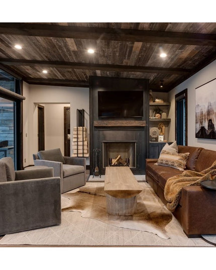 The Toby Firewood Holder by Industrial Farm Co displayed in modern rustic living room with exposed wood beams, stone firep...