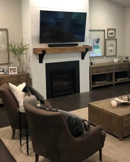 Black metal Kudlick Farmhouse Mantel Brackets supporting wooden shelf above white brick fireplace in modern living room