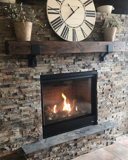 Black metal mantel bracket supporting dark wood beam on stone brick fireplace with flames visible, Industrial Farm Co Buff...