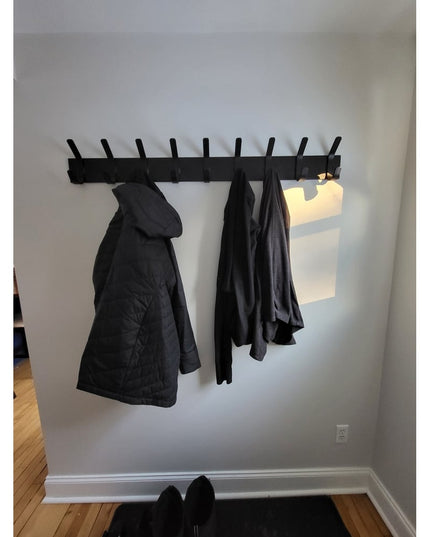 Black wall mounted metal coat rack with 9 hooks holding dark jackets and clothes in modern entryway with wooden floors