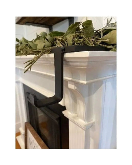 Black metal Annie Stocking Holder by Industrial Farm Co mounted on white fireplace mantel with green holiday garland decor...