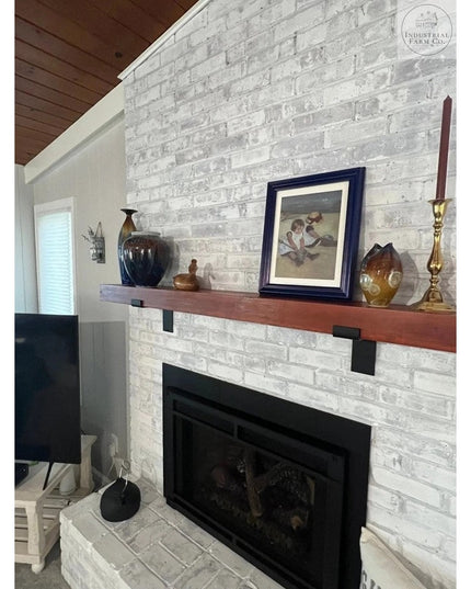 Black metal Z-style shelf brackets supporting wood mantel above white brick fireplace by Industrial Farm Co, displaying ru...