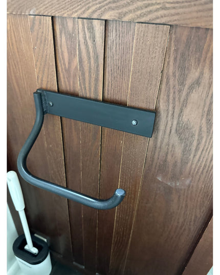 Black metal Howlett Hill toilet paper holder mounted on wood fence with curved arm design by Industrial Farm Co