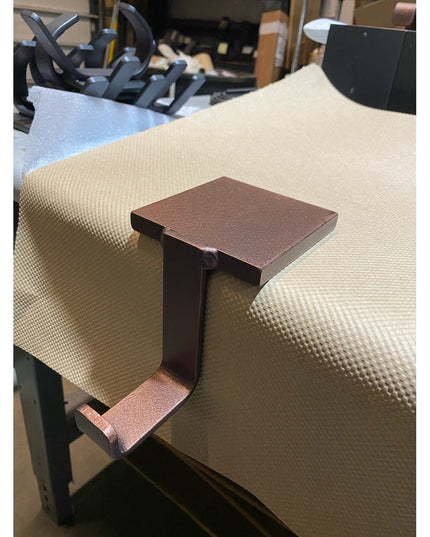 Bronze metal Annie Stocking Holder by Industrial Farm Co clipped onto beige upholstered chair arm in workshop setting