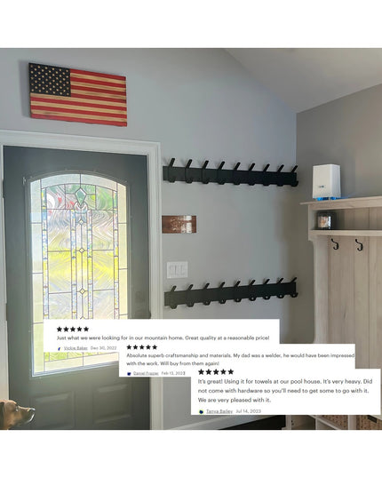 Black metal wall-mounted coat rack with multiple hooks installed in modern entryway with stained glass door and American f...