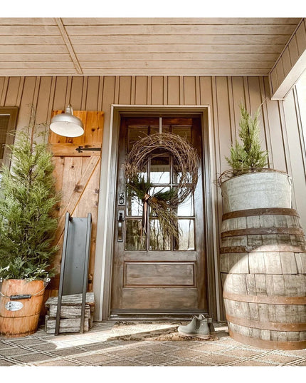 Black metal Toby Firewood Holder by Industrial Farm Co displayed on rustic farmhouse porch with wood door and barrel decor