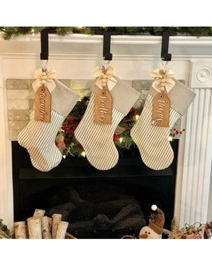 Black metal Annie Stocking Holder by Industrial Farm Co displaying three cream striped Christmas stockings with brown leat...