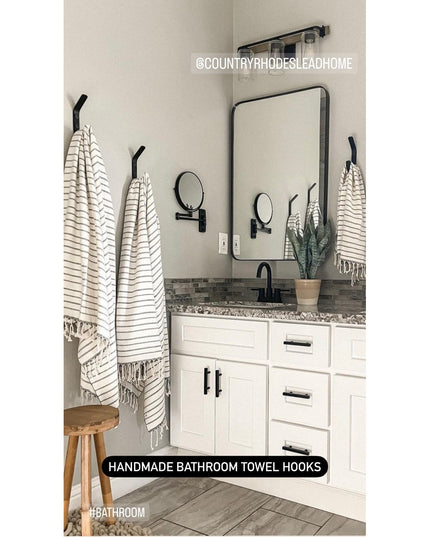 Black metal Henrietta 1" wide double bathroom towel hooks mounted on white wall holding striped towels in modern farmhouse...