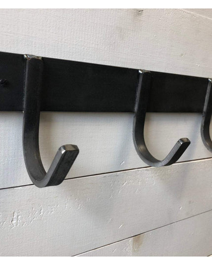 Black metal Camillus Style Coat Rack by Industrial Farm Co with four curved hooks mounted on white shiplap wall