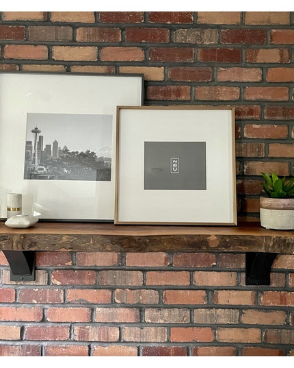 Industrial Farm Co Albany black steel shelf brackets supporting rustic wood mantel with framed artwork and plant on expose...