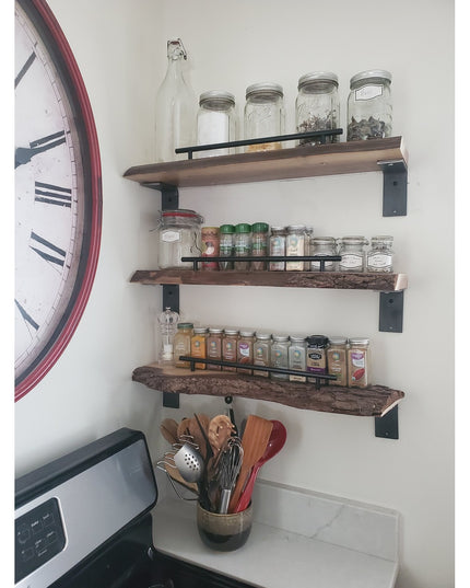 Black steel L-bracket shelf supports holding rustic wood floating shelves with mason jars, spices, and kitchen utensils in...