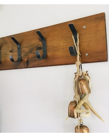 Rustic wooden wall-mounted coat rack with black metal double hooks displaying colorful bags and woven corn husk decoration...