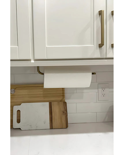 The Hyde Hall Paper Towel Holder by Industrial Farm Co mounted under white kitchen cabinets with brass hardware, showing b...