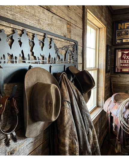 Western Charm black metal coat rack with cowboy silhouette cutout mounted on rustic wood wall, holding brown cowboy hats a...