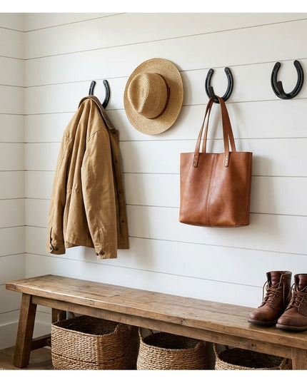 Heavy duty black metal horseshoe wall hooks mounted on white shiplap wall holding jacket, hat and leather bag in rustic fa...
